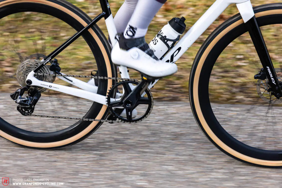 Close-up of a cyclist on a white bicycle with black tires, riding on a road.