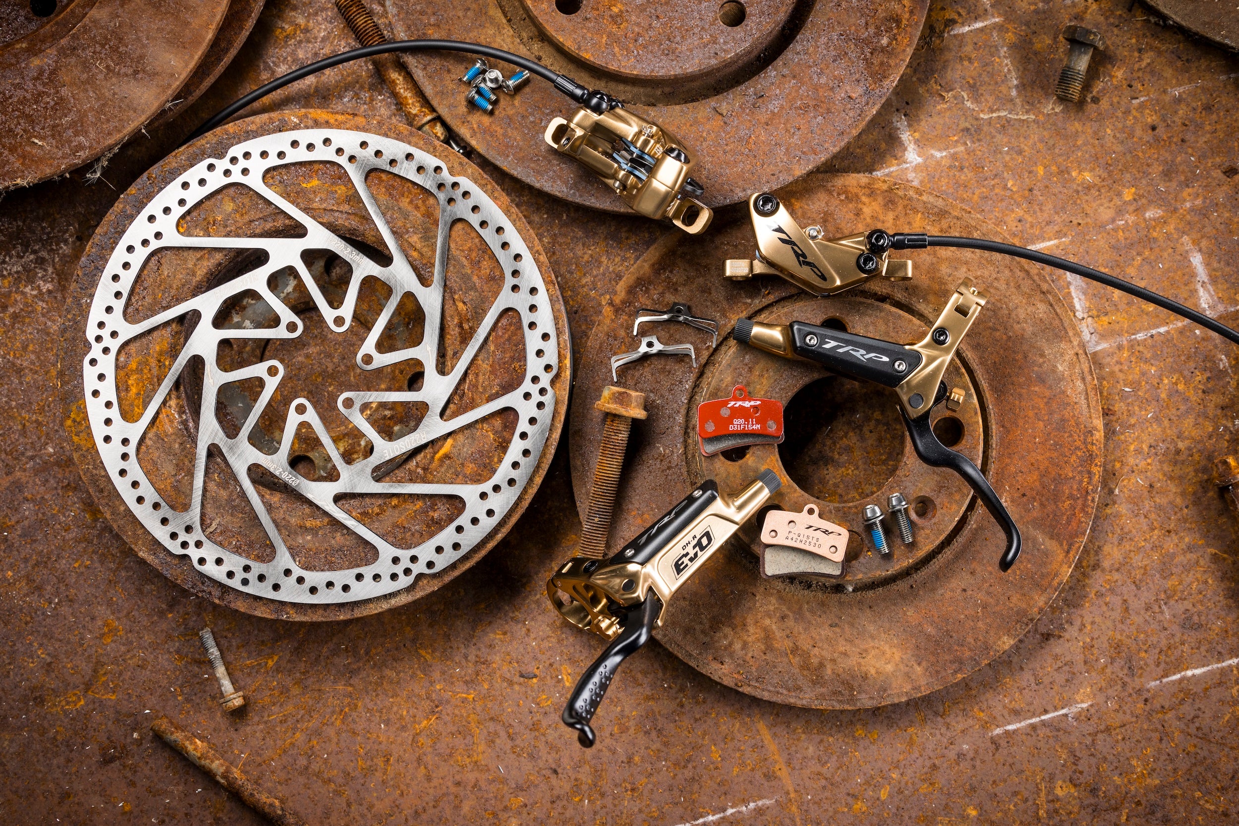 multiple parts of a TRP brake like rotor, caliper, lever, brake pads, and screws laid out in a rusty background