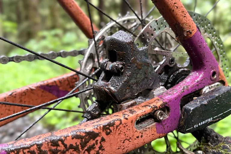 Close-up of a bicycle with a dirty TRP caliper and rotor on a purple and orange frame.