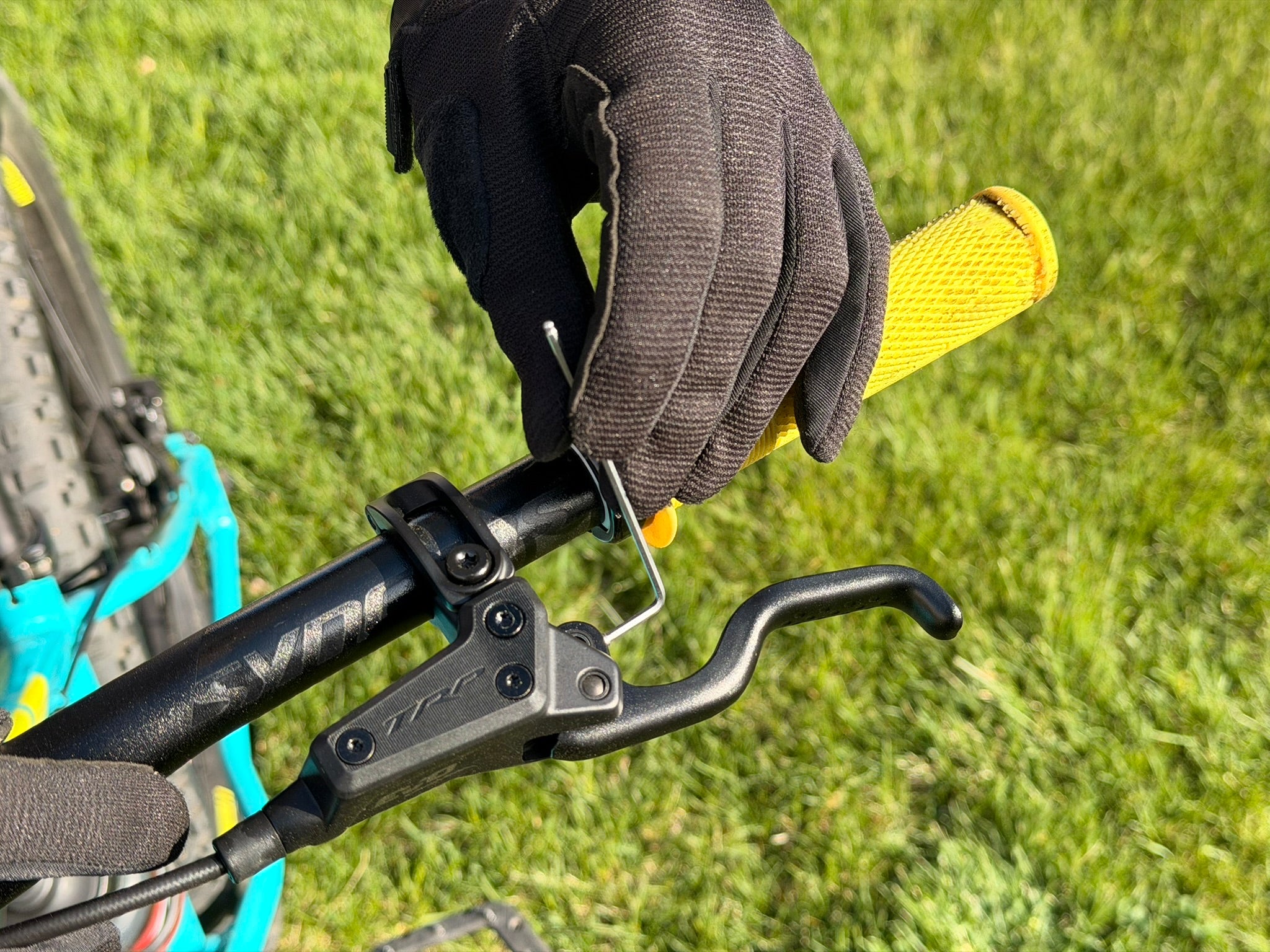 Close-up of a gloved hand adjusting a bicycle brake lever with a grassy background.