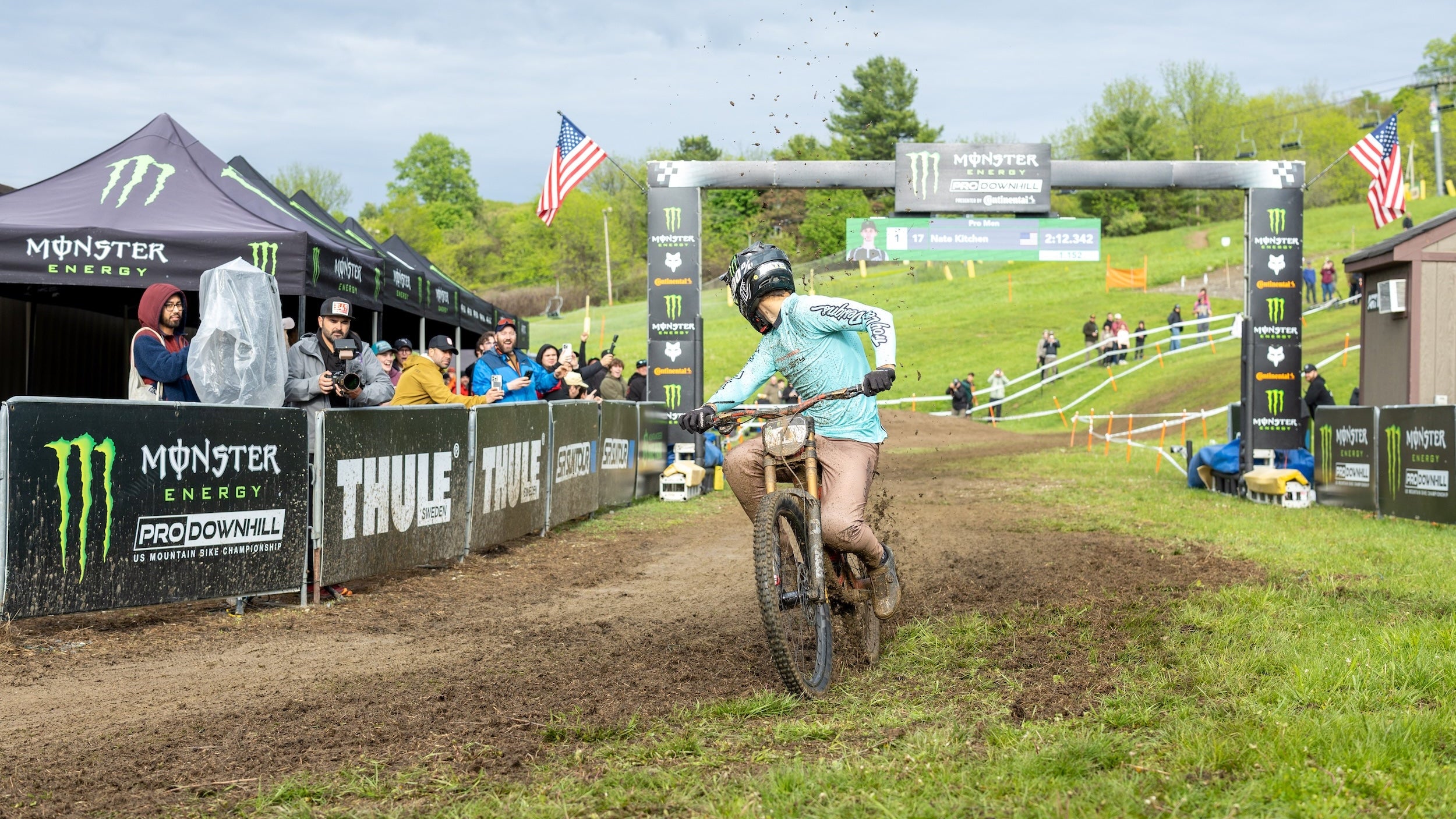 Biker crossing finish line at a mountain biking event with Monster Energy and Thule branding.