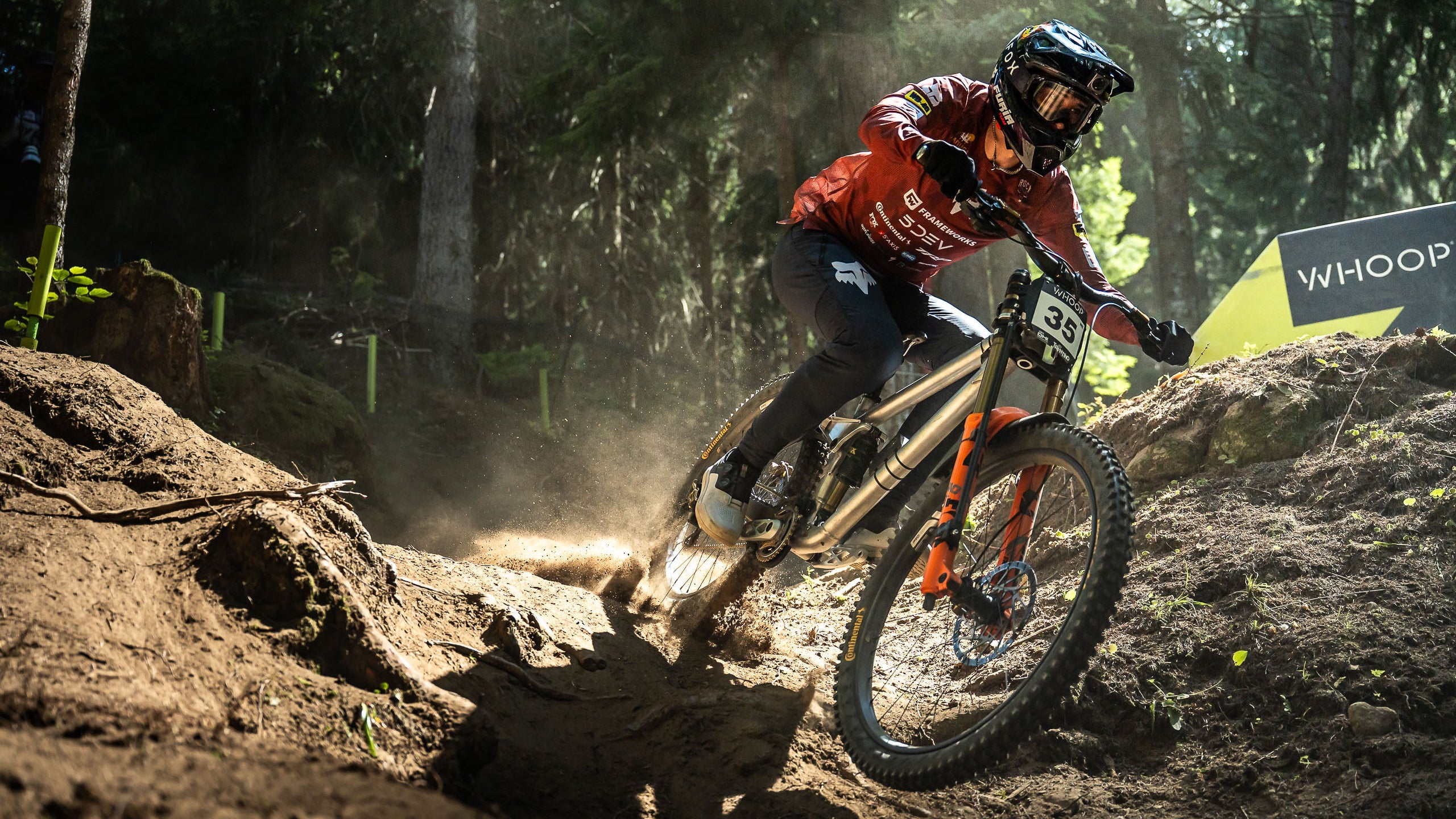 Biker in action on a dirt track with trees and a sign in the background